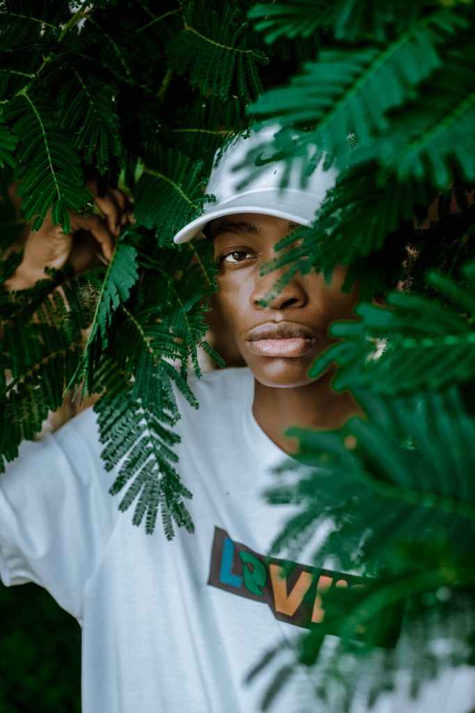 confident young black guy hiding behind plant leaves