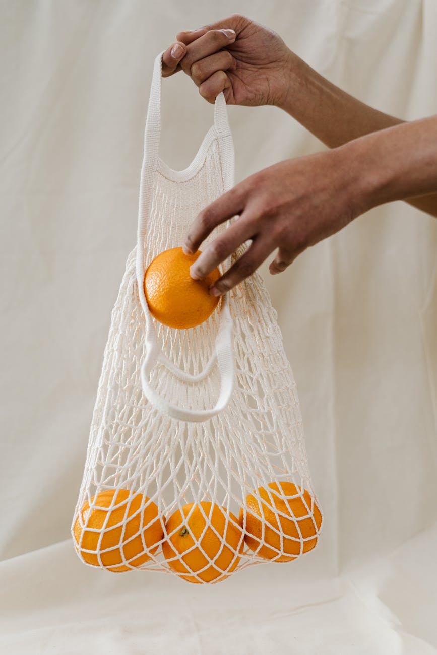 person holding orange fruits in white net